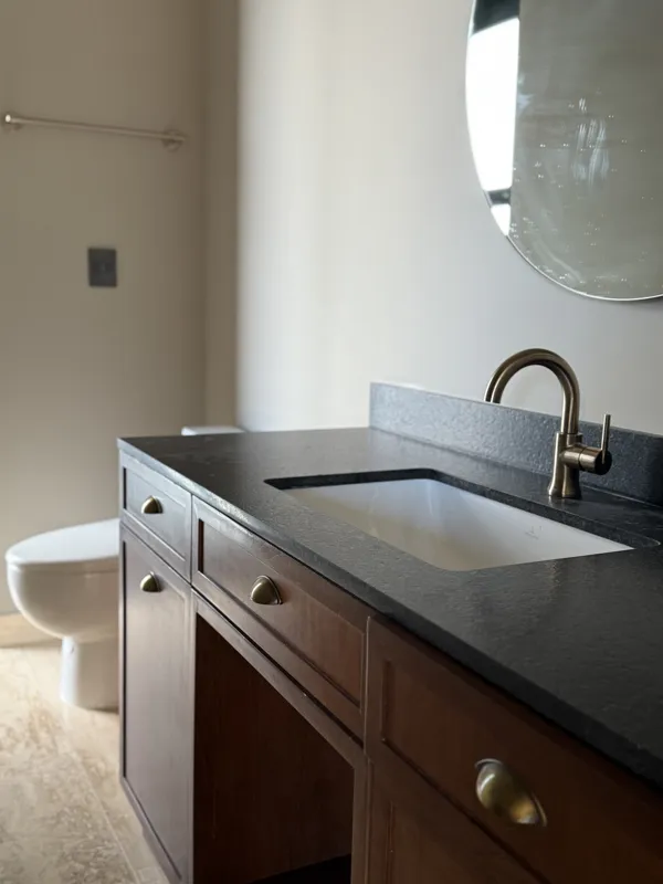A close-up shot of a modern, brushed brass gooseneck faucet with a single lever handle, set against a dark, speckled countertop and a dark grey backsplash, indicating high-quality interior finishes in an Arthouse Signature apartment.