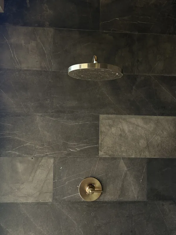 A close-up shot of a modern, brushed brass gooseneck faucet with a single lever handle, set against a dark, speckled countertop and a dark grey backsplash, indicating high-quality interior finishes in an Arthouse Signature apartment.