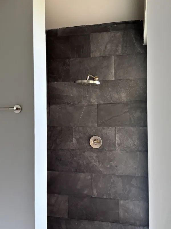 A bright, finished interior room in an Arthouse Signature one-bedroom apartment, featuring light-colored tiled floors, light grey walls, an installed air conditioning unit, and a large sliding glass door opening to a private balcony with lush gree...