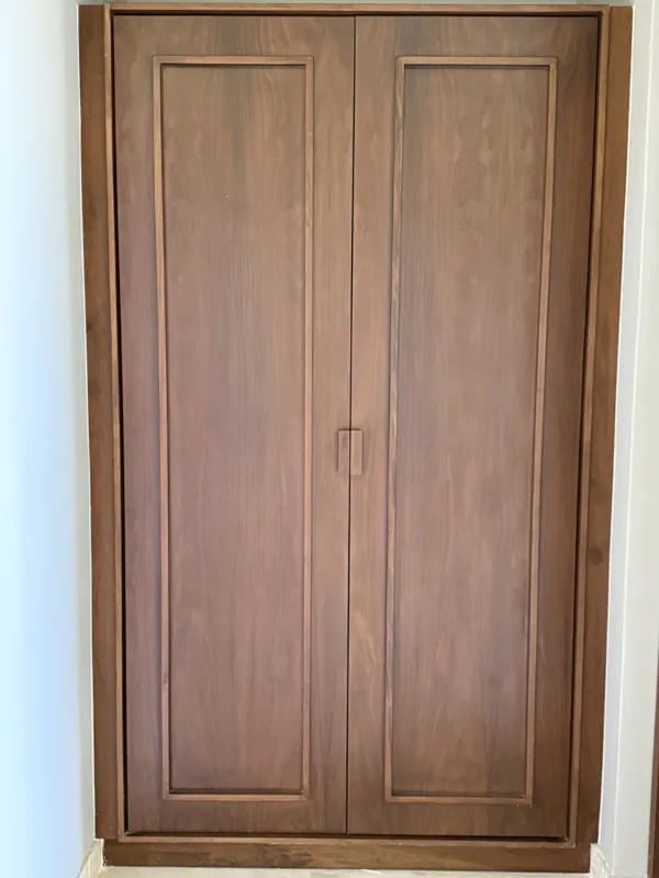 A bright, finished interior room in an Arthouse Signature one-bedroom apartment, featuring light-colored tiled floors, light grey walls, an installed air conditioning unit, and a large sliding glass door opening to a private balcony with lush gree...