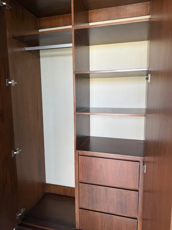 A bright, finished interior room in an Arthouse Signature one-bedroom apartment, featuring light-colored tiled floors, light grey walls, an installed air conditioning unit, and a large sliding glass door opening to a private balcony with lush gree...