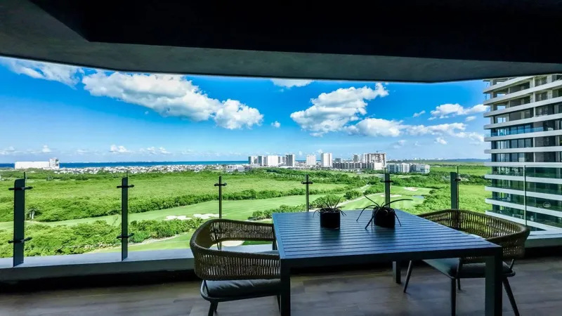 A spacious, elegantly furnished living room in a Woha residence, featuring modern decor, marble floors, and large sliding glass doors opening to a private terrace with panoramic views of the natural reserve, golf course, and distant Caribbean Sea.