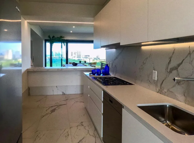 A spacious, elegantly furnished living room in a Woha residence, featuring modern decor, marble floors, and large sliding glass doors opening to a private terrace with panoramic views of the natural reserve, golf course, and distant Caribbean Sea.