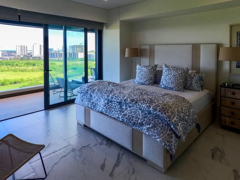 A spacious, elegantly furnished living room in a Woha residence, featuring modern decor, marble floors, and large sliding glass doors opening to a private terrace with panoramic views of the natural reserve, golf course, and distant Caribbean Sea.