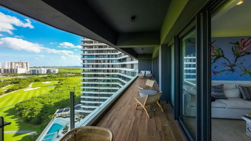 A spacious, elegantly furnished living room in a Woha residence, featuring modern decor, marble floors, and large sliding glass doors opening to a private terrace with panoramic views of the natural reserve, golf course, and distant Caribbean Sea.