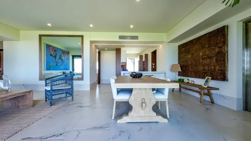 A spacious, elegantly furnished living room in a Woha residence, featuring modern decor, marble floors, and large sliding glass doors opening to a private terrace with panoramic views of the natural reserve, golf course, and distant Caribbean Sea.