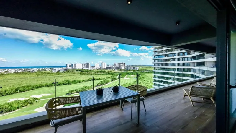 A spacious, elegantly furnished living room in a Woha residence, featuring modern decor, marble floors, and large sliding glass doors opening to a private terrace with panoramic views of the natural reserve, golf course, and distant Caribbean Sea.