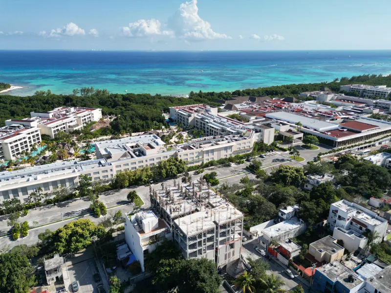 Aerial view of the Maia development construction site in Playa del Carmen, showing multiple concrete columns with rebar and wooden formwork being erected on the upper levels, indicating active progress on the 7th floor, with construction workers v...