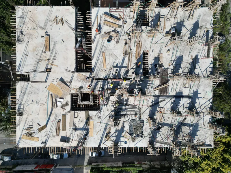 Aerial view of the Maia development construction site in Playa del Carmen, showing multiple concrete columns with rebar and wooden formwork being erected on the upper levels, indicating active progress on the 7th floor, with construction workers v...