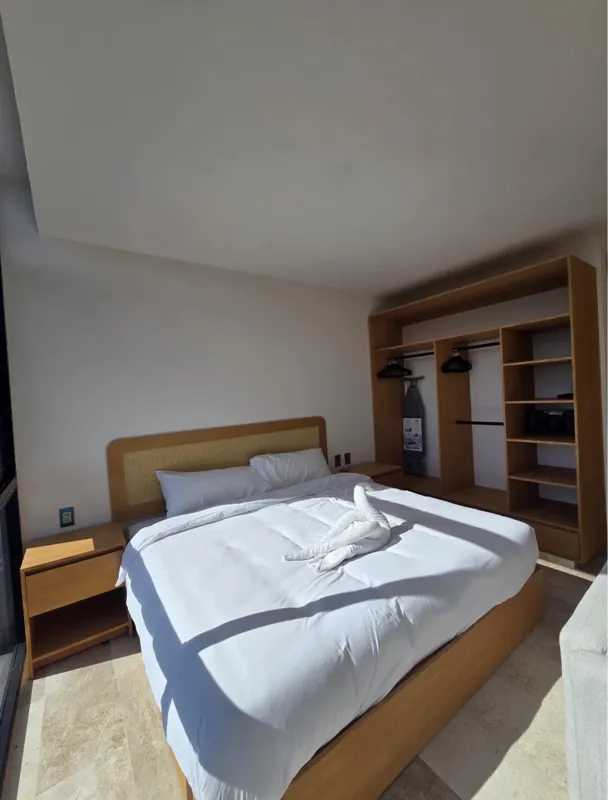 A bright, modern bathroom in an Akua Signature model unit, featuring a floating light wood vanity with a white vessel sink, a large rectangular mirror, a white toilet with a small towel animal, and a spacious walk-in shower with a glass enclosure ...