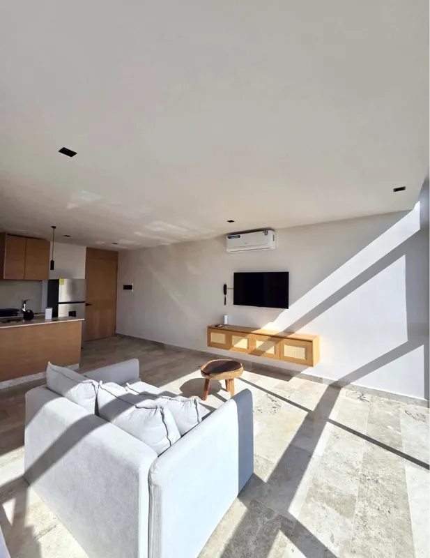 A bright, modern bathroom in an Akua Signature model unit, featuring a floating light wood vanity with a white vessel sink, a large rectangular mirror, a white toilet with a small towel animal, and a spacious walk-in shower with a glass enclosure ...