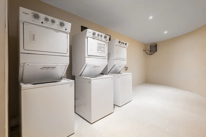Aerial view of the Peregrina development in Tulum, showing multiple completed buildings with white facades, rooftop gardens, and a visible rooftop pool, surrounded by dense green jungle foliage under a blue sky with white clouds. The ocean is visi...