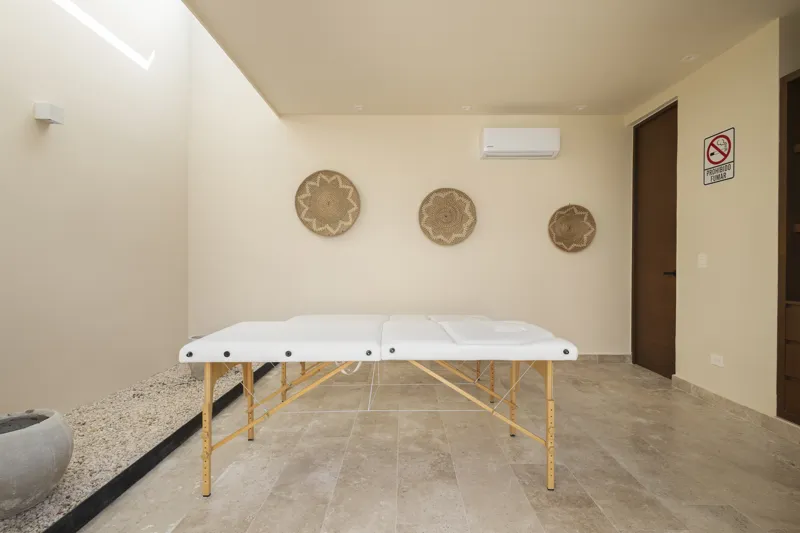 Aerial view of the Peregrina development in Tulum, showing multiple completed buildings with white facades, rooftop gardens, and a visible rooftop pool, surrounded by dense green jungle foliage under a blue sky with white clouds. The ocean is visi...