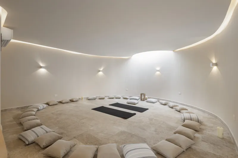 Aerial view of the Peregrina development in Tulum, showing multiple completed buildings with white facades, rooftop gardens, and a visible rooftop pool, surrounded by dense green jungle foliage under a blue sky with white clouds. The ocean is visi...