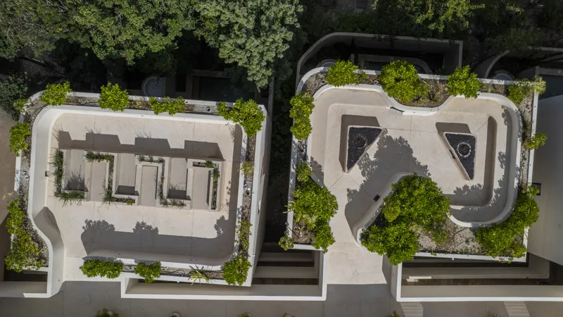 Aerial view of the Peregrina development in Tulum, showing multiple completed buildings with white facades, rooftop gardens, and a visible rooftop pool, surrounded by dense green jungle foliage under a blue sky with white clouds. The ocean is visi...