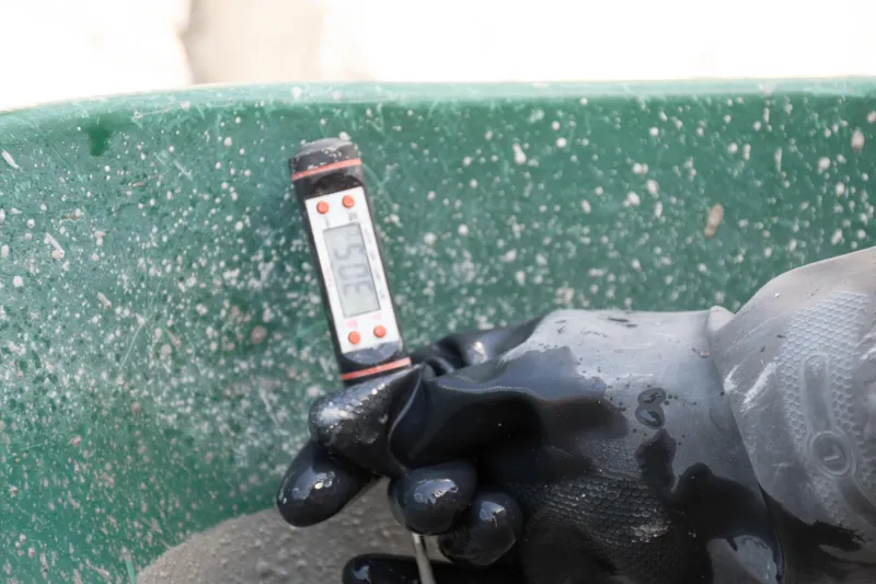 An elevated view of the Abund construction site in Riviera Maya, showing a large white 'Parma' concrete pump truck with its boom extended, actively pouring concrete into a vast, newly formed structural slab. Numerous construction workers in safety...