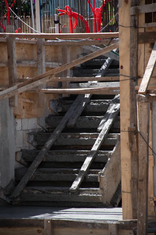 An elevated view of the Abund construction site in Riviera Maya, showing a large white 'Parma' concrete pump truck with its boom extended, actively pouring concrete into a vast, newly formed structural slab. Numerous construction workers in safety...