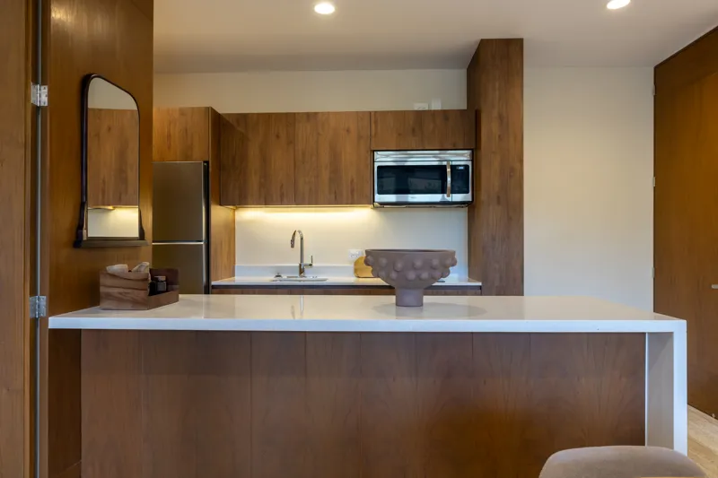 An interior view of Constelada's 1-bedroom model unit, showcasing a modern living and dining area. The space features a light grey sofa with decorative pillows, a sculptural white coffee table, and a round wooden dining table with four light grey ...
