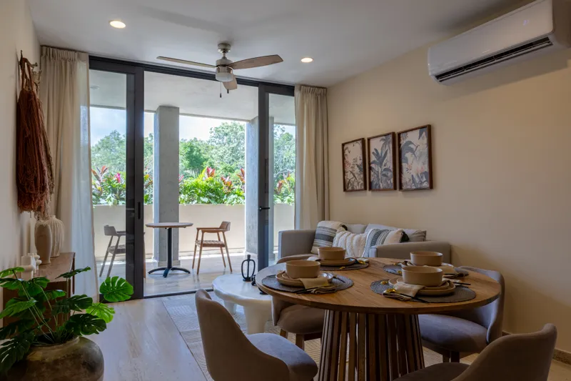 An interior view of Constelada's 1-bedroom model unit, showcasing a modern living and dining area. The space features a light grey sofa with decorative pillows, a sculptural white coffee table, and a round wooden dining table with four light grey ...