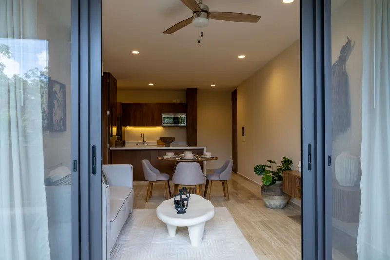 An interior view of Constelada's 1-bedroom model unit, showcasing a modern living and dining area. The space features a light grey sofa with decorative pillows, a sculptural white coffee table, and a round wooden dining table with four light grey ...
