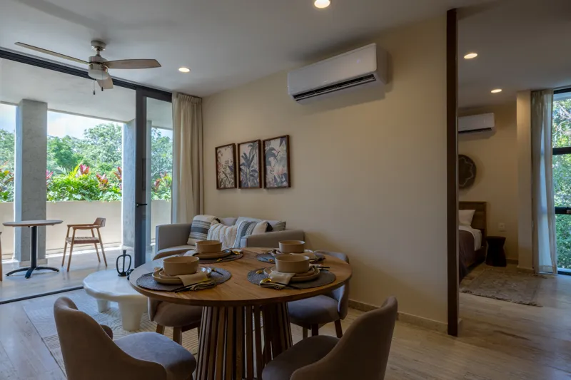 An interior view of Constelada's 1-bedroom model unit, showcasing a modern living and dining area. The space features a light grey sofa with decorative pillows, a sculptural white coffee table, and a round wooden dining table with four light grey ...