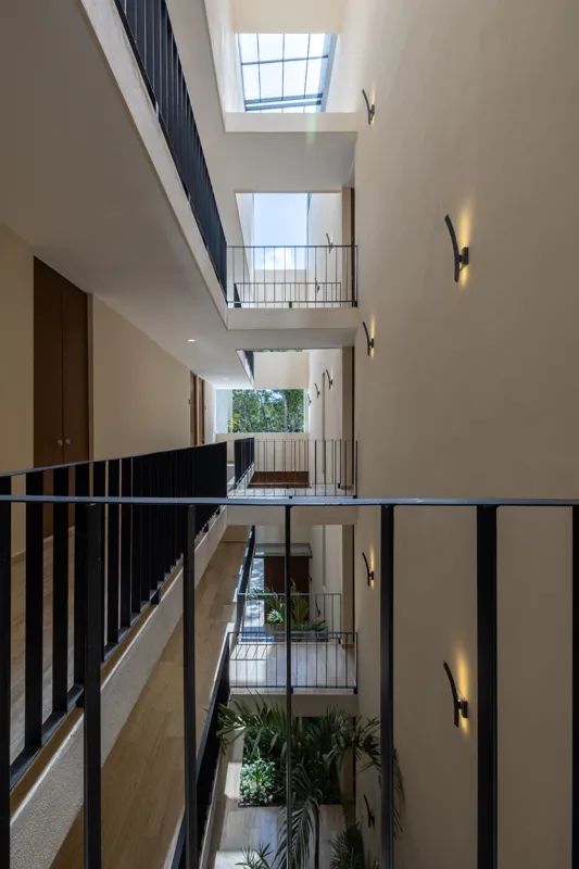 A fully completed and furnished rooftop amenity area at Constelada, featuring a dark-tiled pool with integrated wooden decking, comfortable light-colored beanbag chairs, and lush tropical plants, all set against a vibrant blue sky with white cloud...