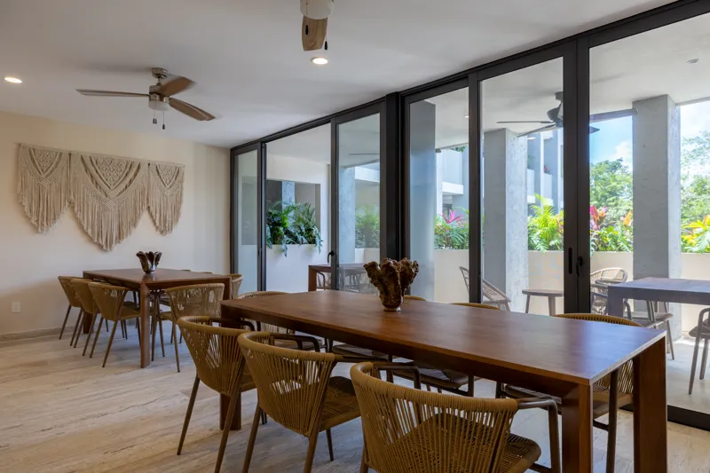 A fully completed and furnished rooftop amenity area at Constelada, featuring a dark-tiled pool with integrated wooden decking, comfortable light-colored beanbag chairs, and lush tropical plants, all set against a vibrant blue sky with white cloud...