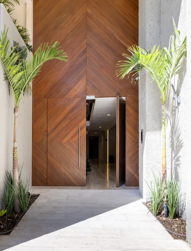 A fully completed and furnished rooftop amenity area at Constelada, featuring a dark-tiled pool with integrated wooden decking, comfortable light-colored beanbag chairs, and lush tropical plants, all set against a vibrant blue sky with white cloud...