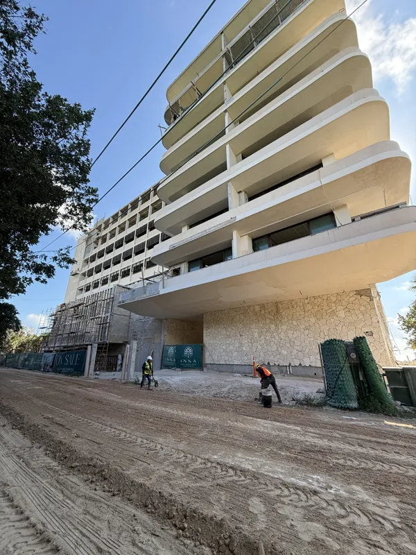 A multi-story building under active construction for INNA Condos in Puerto Morelos. The lower levels of the modern section feature newly applied light-colored stone cladding and installed windows. Above, multiple floors display structurally comple...