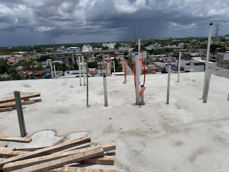 Panoramic view from the newly completed upper-level concrete slab at Ola de Mar, showcasing the urban landscape of Playa del Carmen, including a large commercial building, and the distant Caribbean Sea under a blue sky with white clouds. Construct...