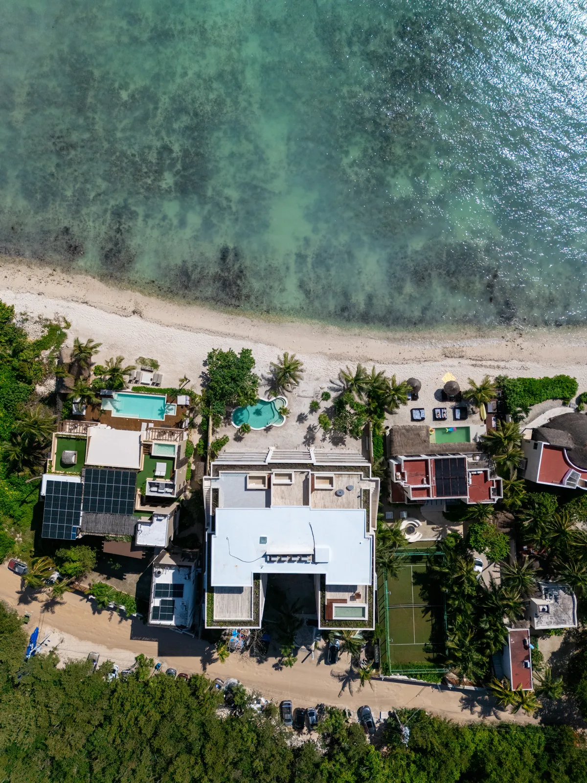 Aerial view of beachfront villas with pools and tennis court