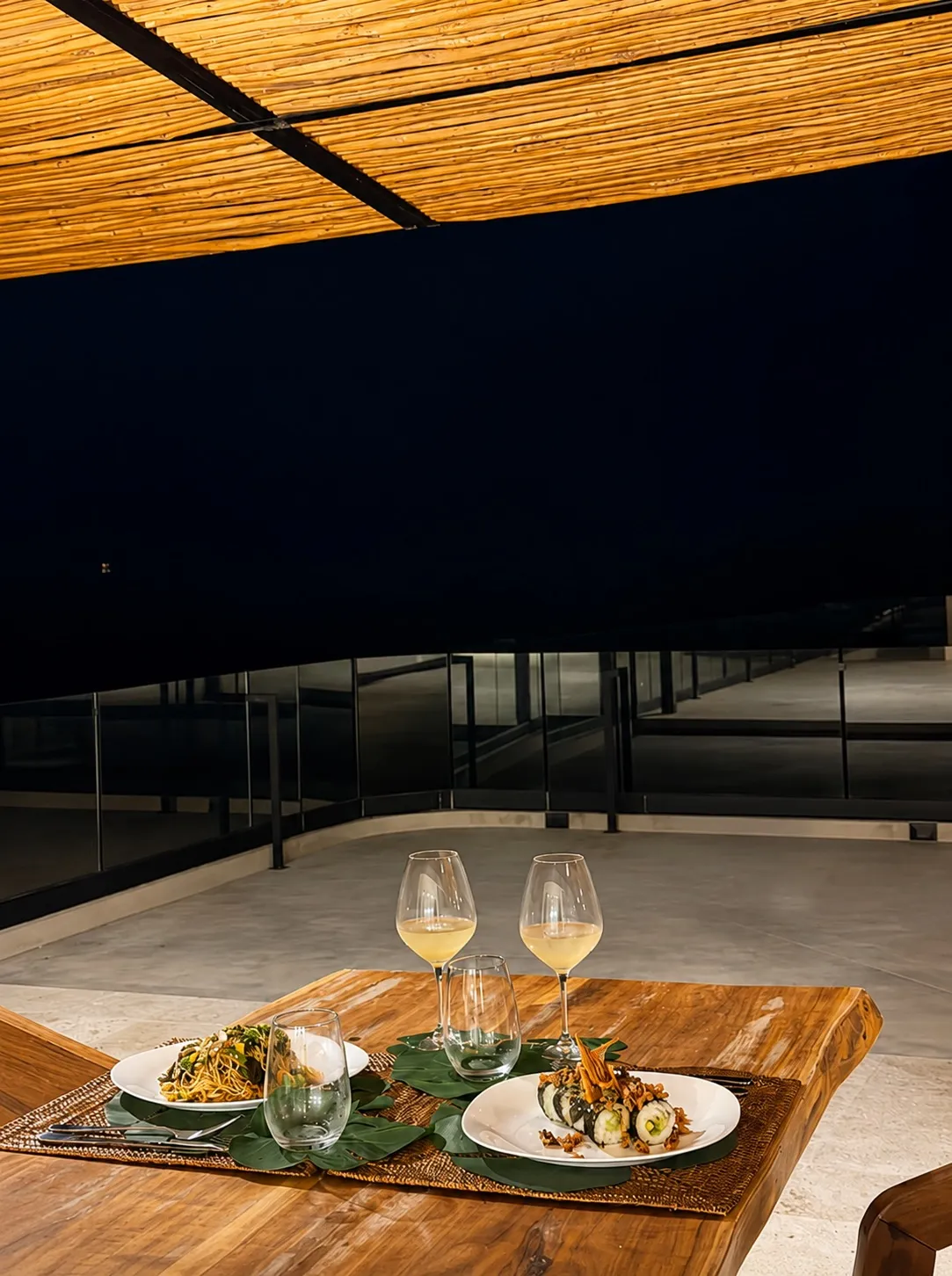Dining table with food and wine on a rooftop terrace at night.