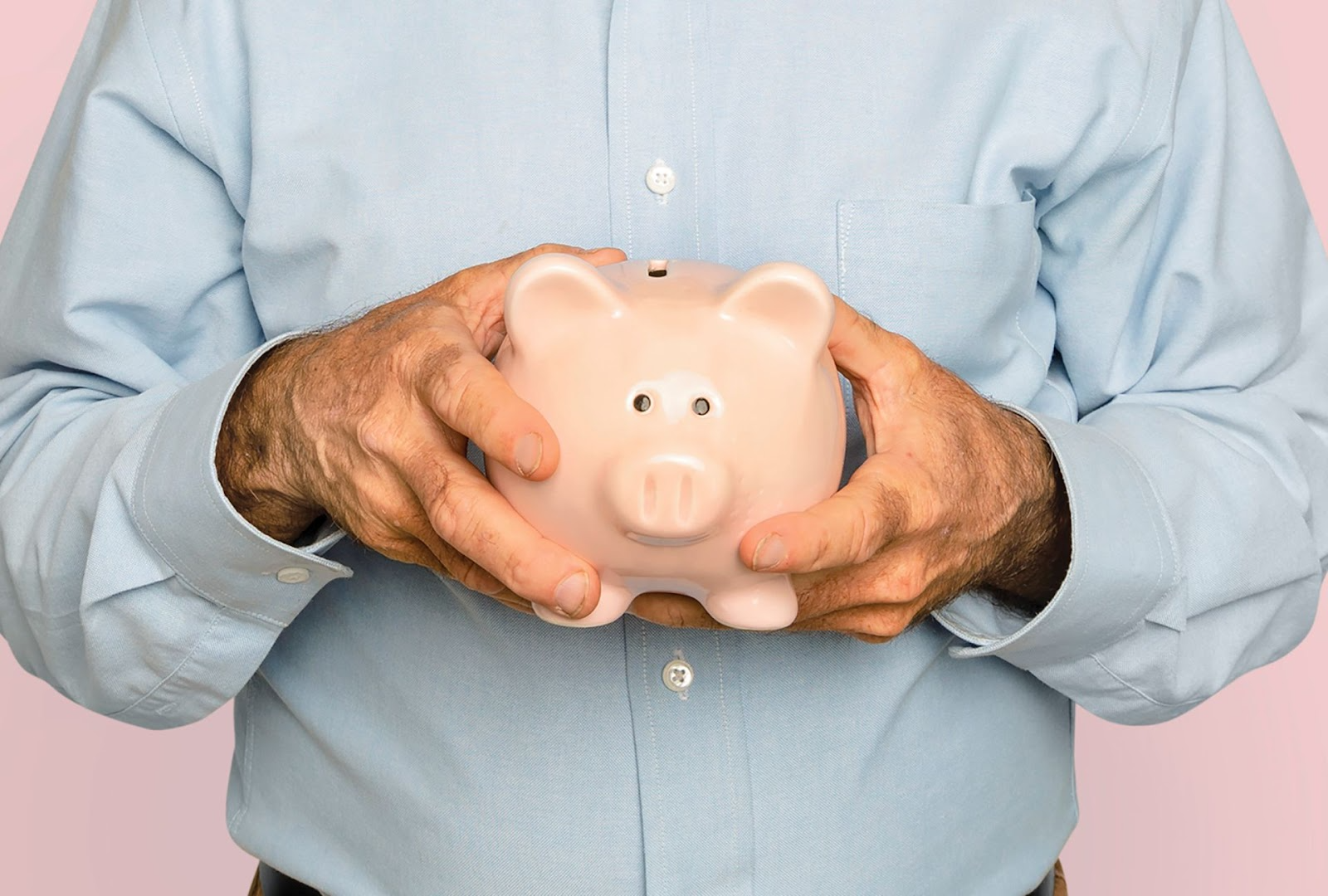 Hombre protegiendo alcancía rosa con las manos, simbolizando ahorro y protección financiera