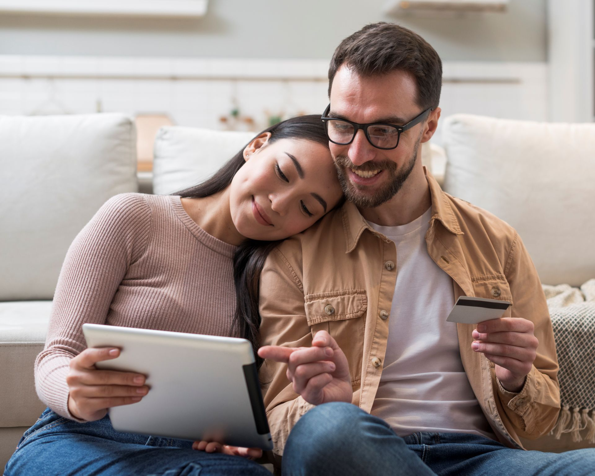 Pareja relajada y sonriente en sofá revisando tablet y tarjeta de crédito