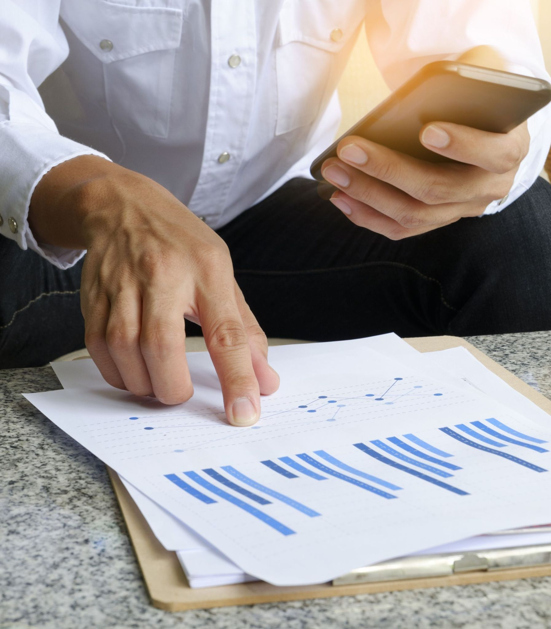 Persona analizando gráficos financieros en papel mientras usa smartphone