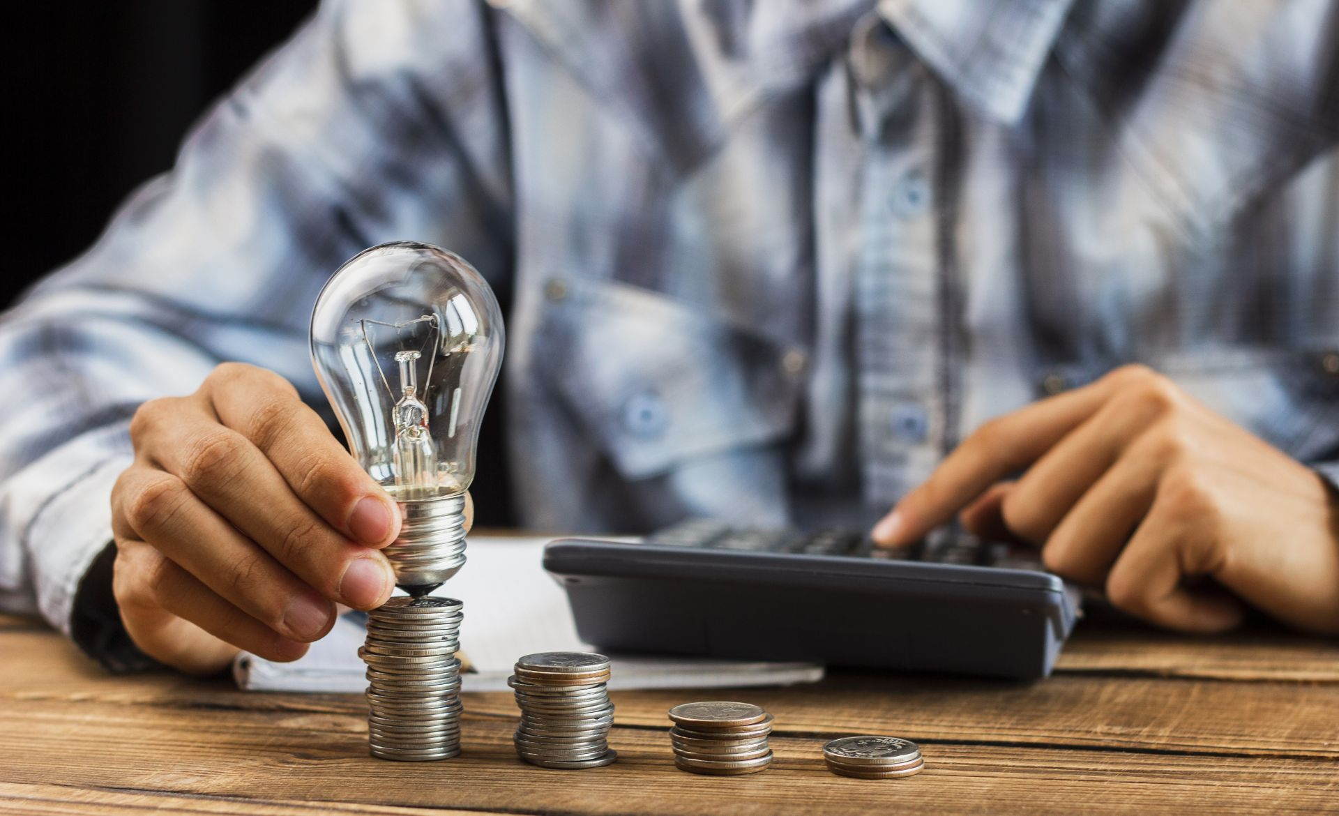 Empresario sosteniendo bombilla sobre monedas apiladas calculando gastos mensuales