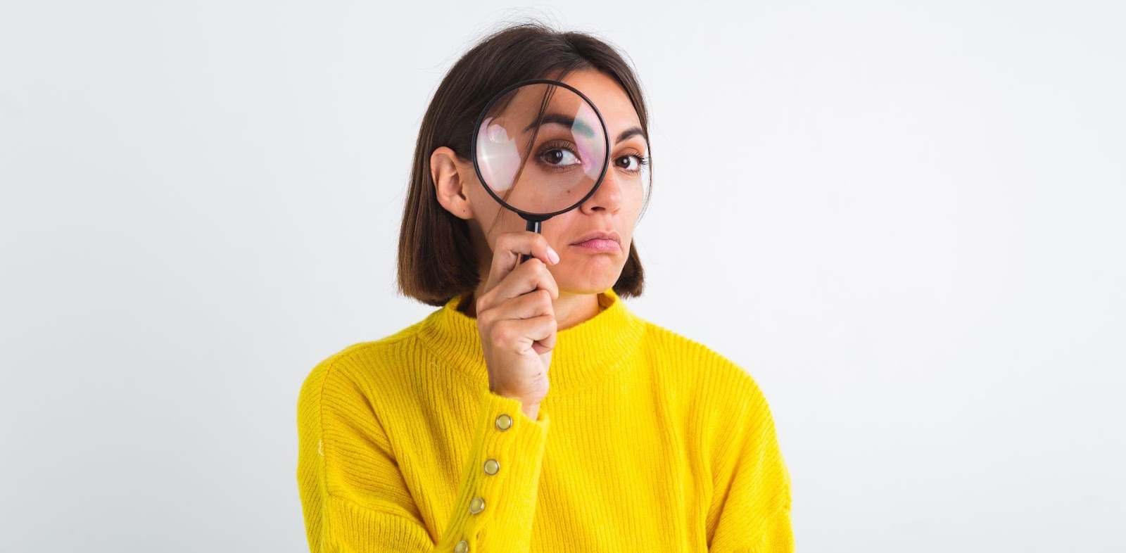 Mujer con suéter amarillo mirando a través de lupa simbolizando investigación y análisis financiero