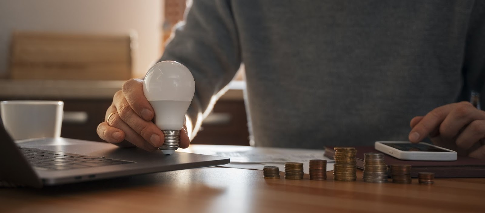 Persona sosteniendo bombilla LED junto a monedas apiladas representando ahorro e inversión inteligente