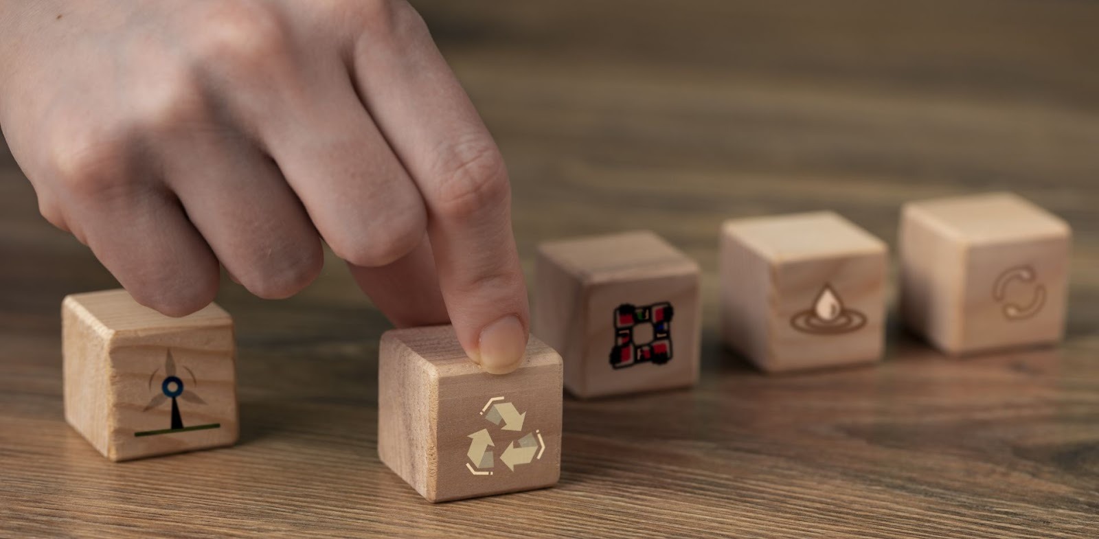Mano seleccionando cubo con símbolo de reciclaje entre bloques de madera con diversos iconos