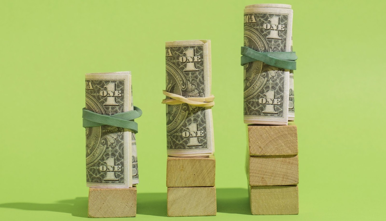 Tres columnas de billetes enrollados sobre bloques ilustrando diferentes niveles de inversión