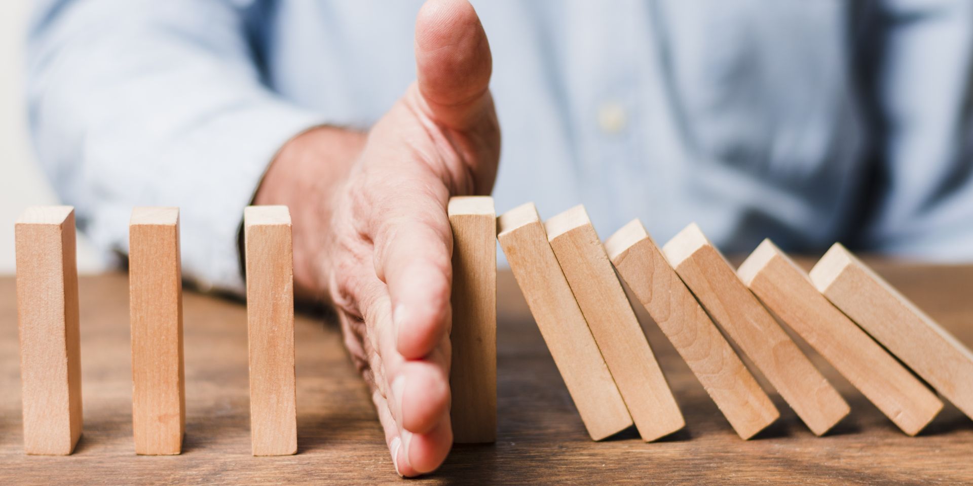 Mano deteniendo fichas de dominó simbolizando protección financiera y gestión de riesgos patrimoniales