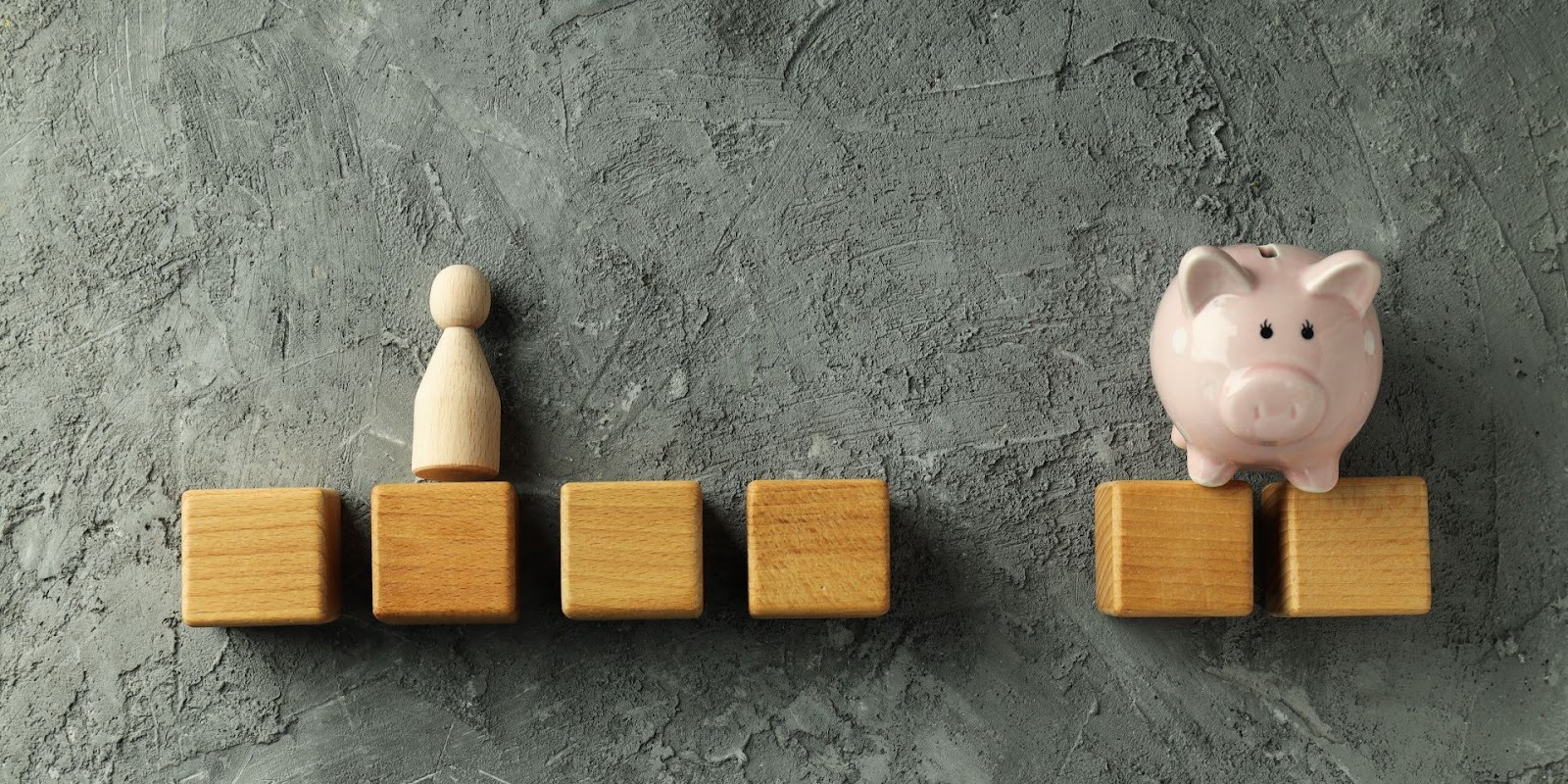 Figura de madera y alcancía sobre bloques simbolizando balance entre personas e inversión de impacto social