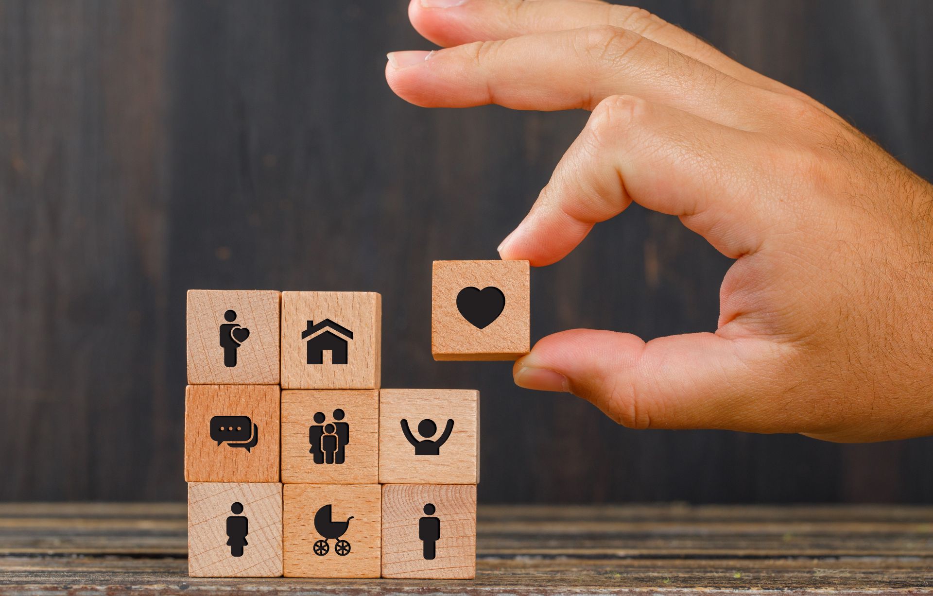 Mano colocando bloque de corazón sobre cubos con íconos de seguros, salud, hogar y familia