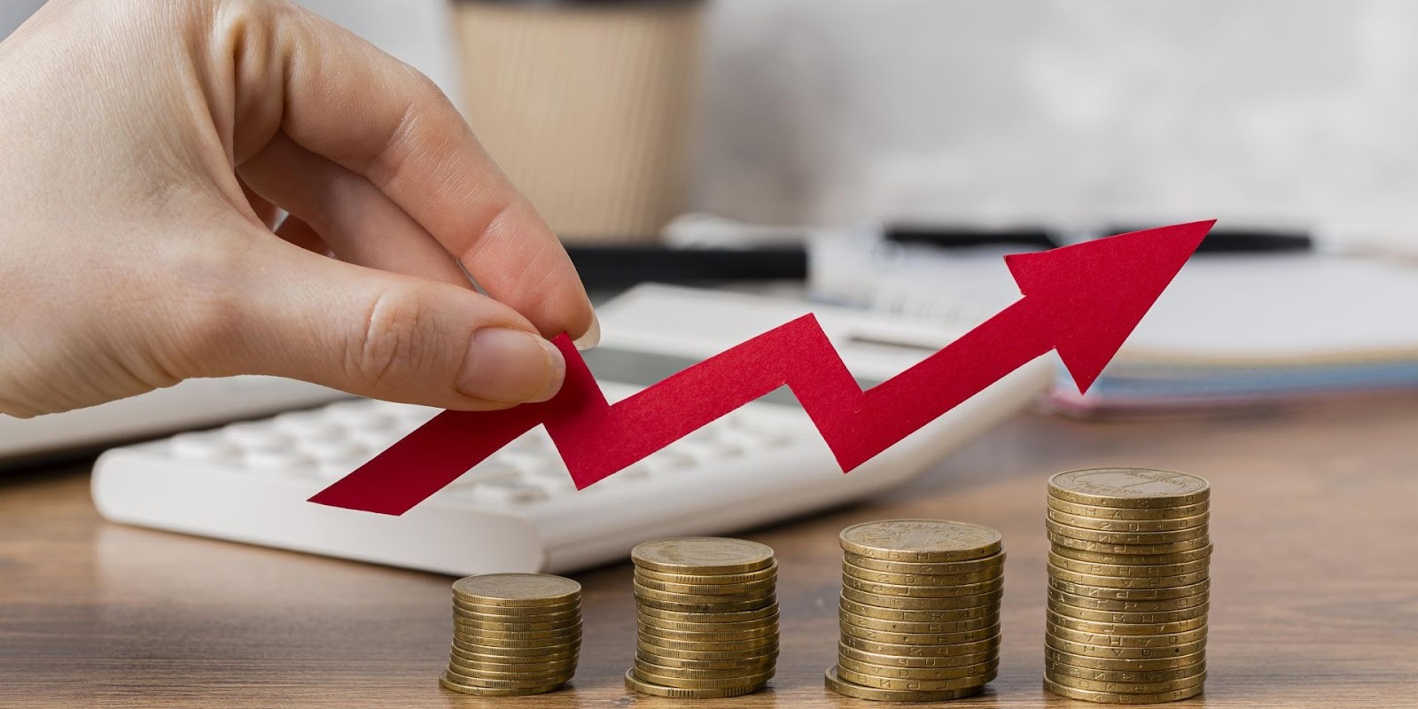 Mano sosteniendo flecha roja de crecimiento sobre pilas de monedas mostrando importancia de plan de inversión