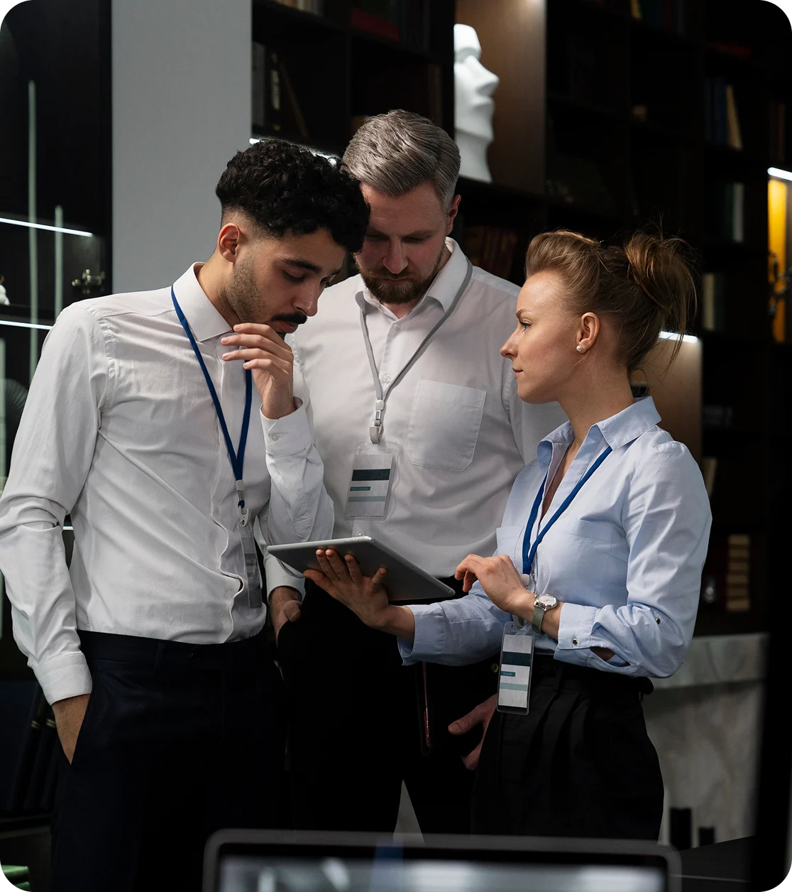 Three professionals in office setting closely reviewing information on a tablet.