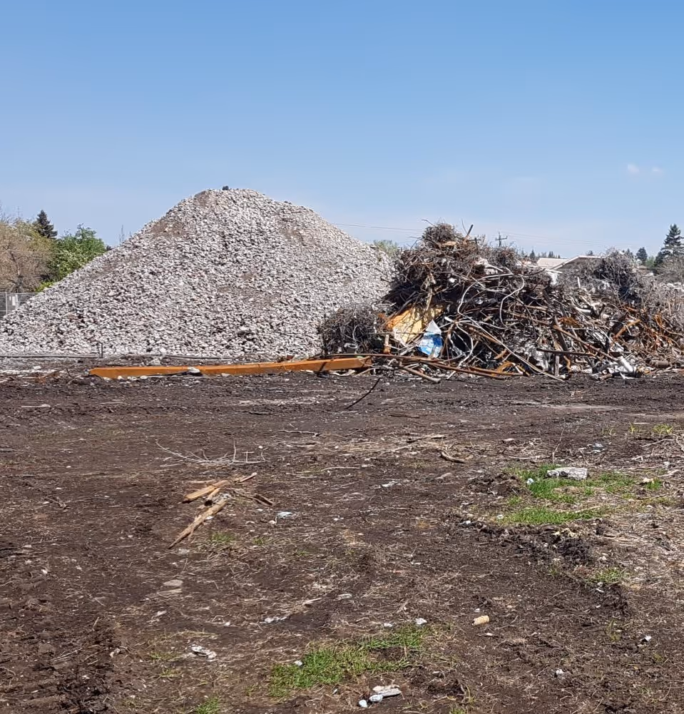 Large piles of construction debris including rubble and metal scrap on a dirt ground under a clear blue sky.