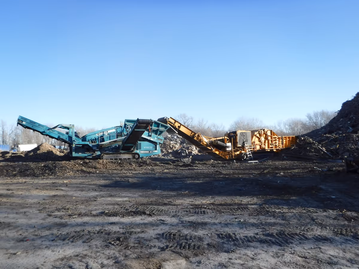 Two large industrial machines with conveyor belts processing soil or debris under a clear blue sky.
