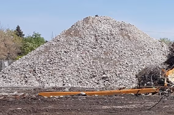 Large pile of crushed concrete or rubble at a construction or demolition site with clear sky and some trees in the background.