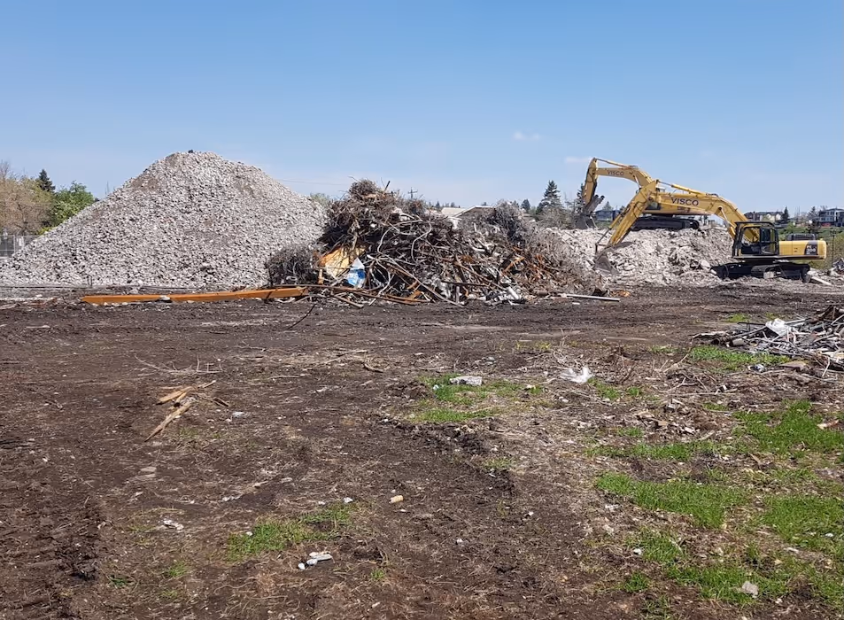 Construction site with two yellow excavators moving large piles of rubble and scrap debris under a clear blue sky.