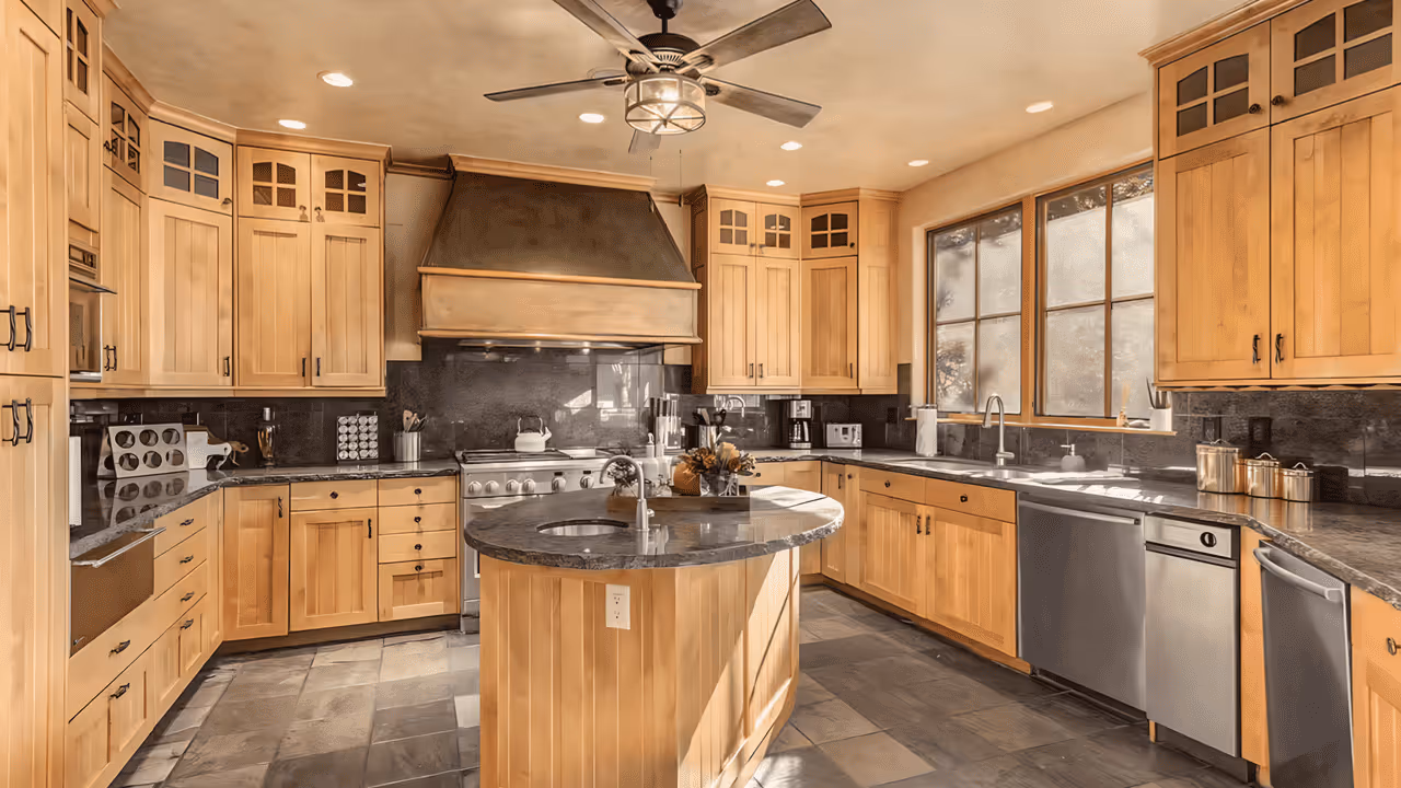 Spacious kitchen with natural wood cabinets, a central island with sink, stainless steel appliances, large windows, and a ceiling fan.